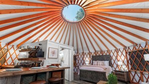 A yurt interior with a central circular skylight, a kitchen area, a bed, and a seating area.