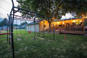 A backyard with a swing set, a small shed, and a house with a porch. - Centrally located, huge shaded patio with fire pit! Entire place to yourself! (Billings)