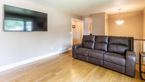 Een woonkamer met een bruine leren bank, een flatscreen televisie aan de muur en een houten vloer.