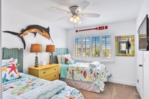 A bedroom with two beds, a ceiling fan, a window with blinds, and a mounted TV. - Headline (St. Augustine)