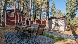 A covered patio with a patterned rug, a dining table with chairs, and a red building in the background. - Vanderhut Chalet (Sugarloaf)