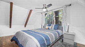A bedroom with a bed, a nightstand, a ceiling fan, a window with curtains, and a wooden floor. - Vanderhut Chalet (Sugarloaf)