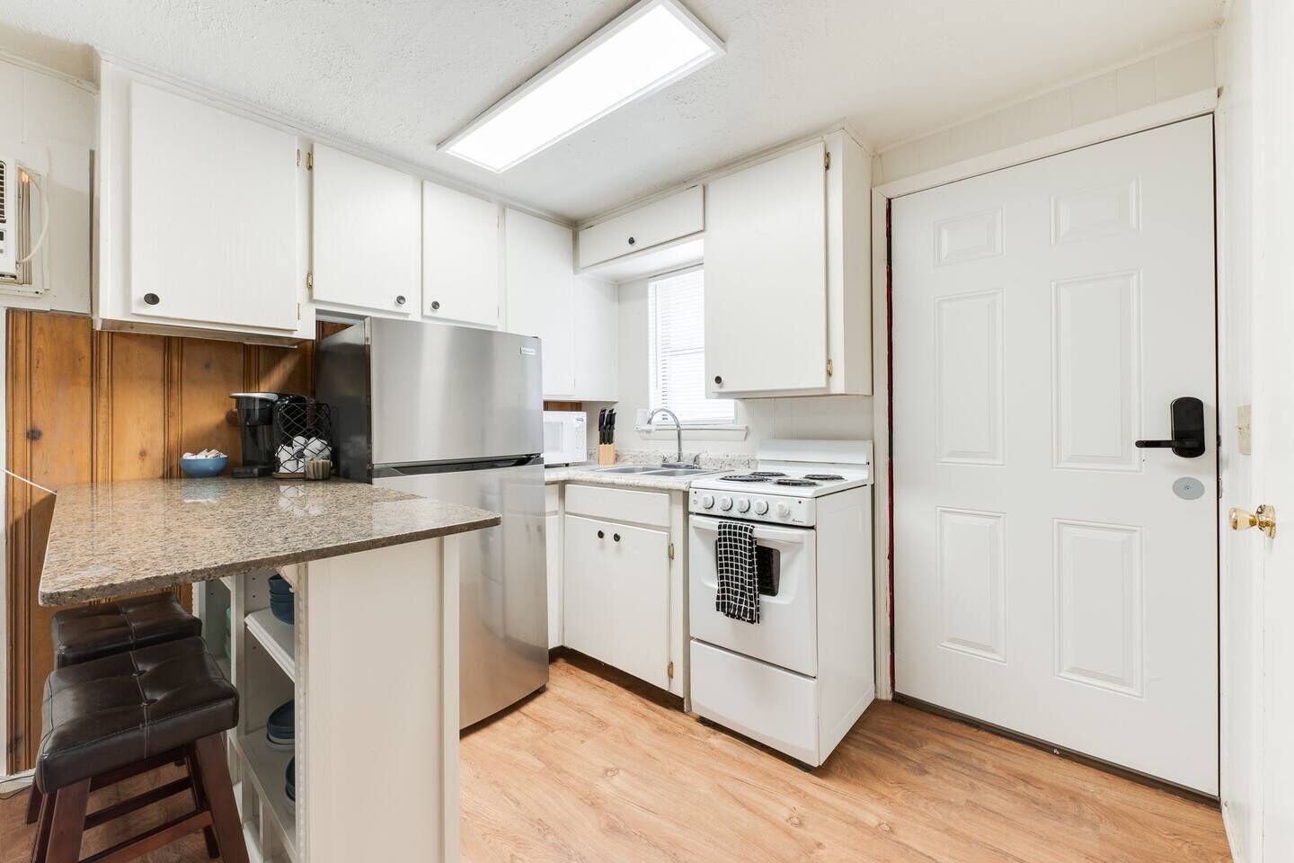 A compact kitchen with white cabinets, a stainless steel refrigerator, a white stove, and a wooden countertop.