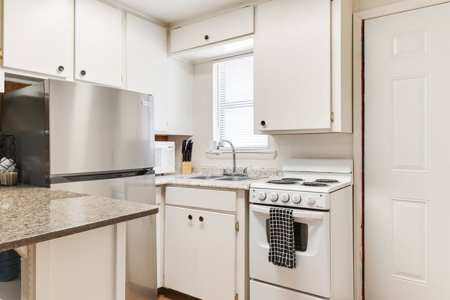 Una cocina compacta con armarios blancos, un refrigerador de acero inoxidable, un microondas, un fregadero y una estufa.