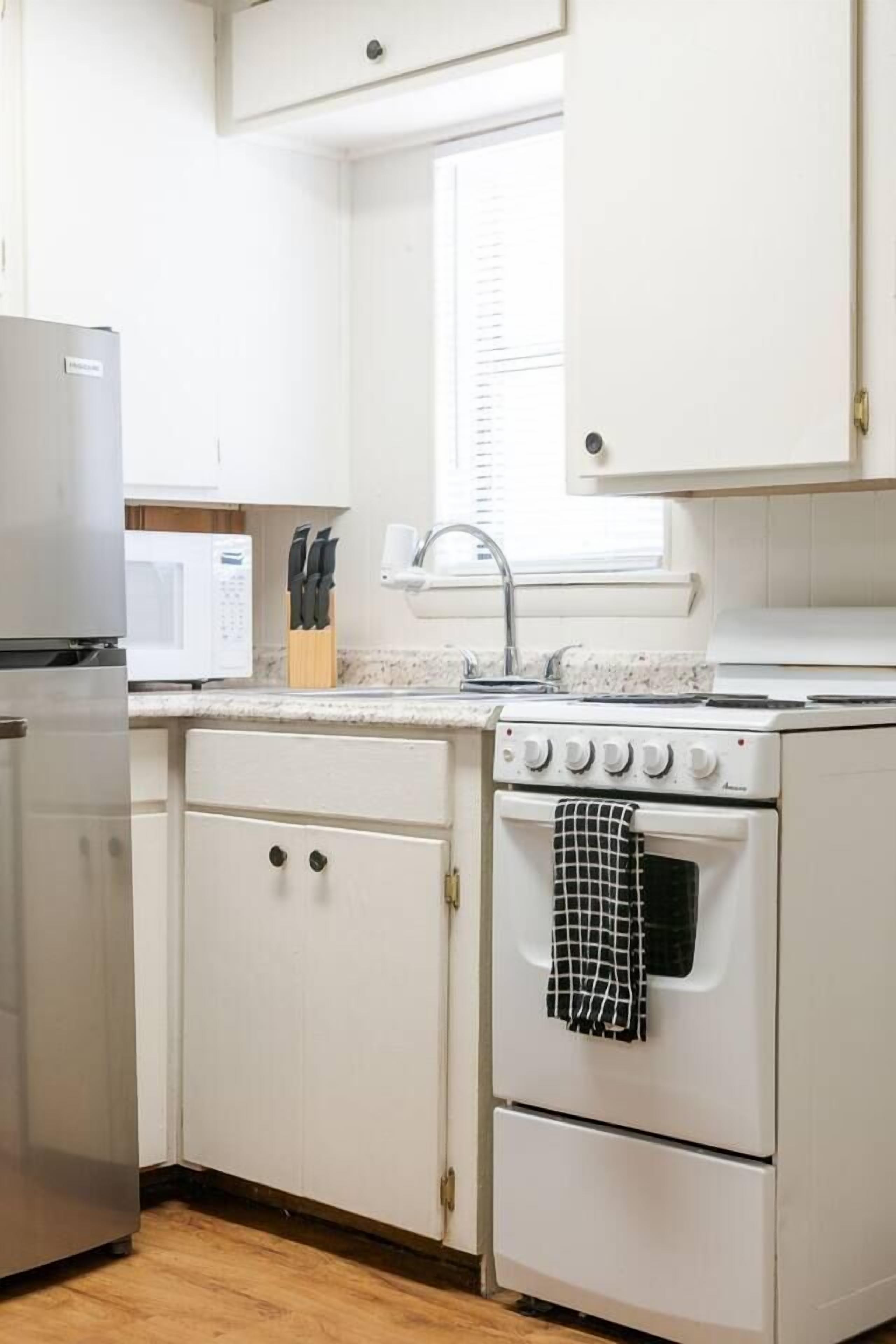 A kitchen with white cabinets, a microwave, a stove, and a sink.