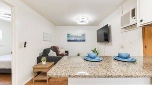 Una cocina compacta con encimera de granito, dos cuencos azules, una pequeña planta y un televisor montado.