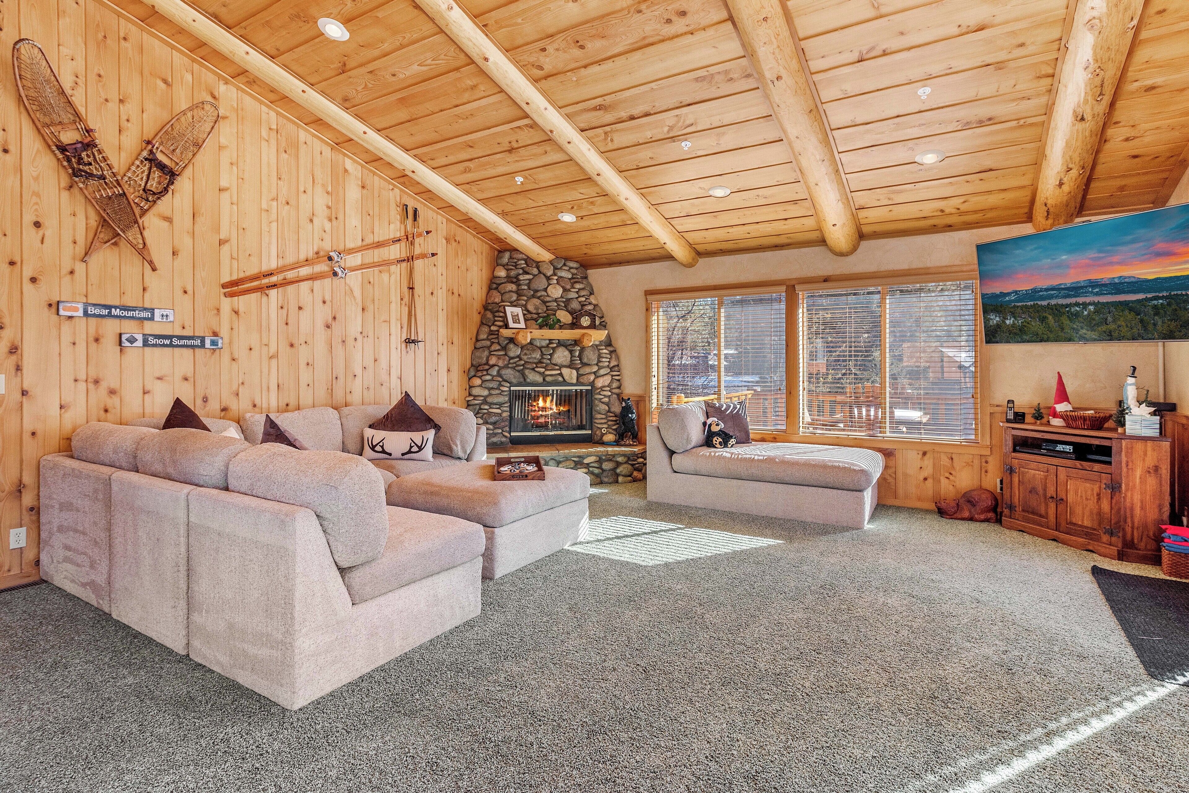 A cozy living room with a stone fireplace, two sofas, and a large window with a view of the outdoors.