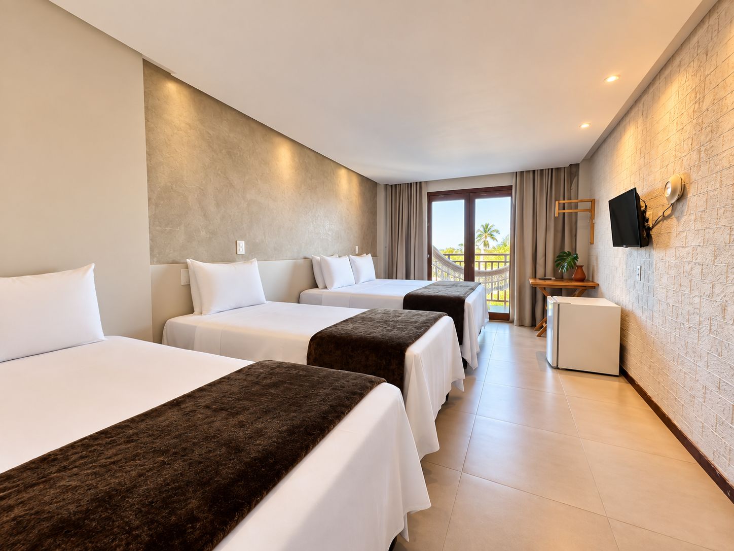Habitación de hotel con dos camas, un escritorio pequeño, un televisor y un balcón con vistas.