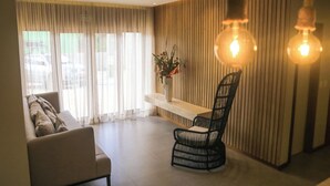 A modern living room with a sofa, a black chair, a wooden wall, and a vase with flowers. - HOTEL ICARAI BEACH (Amontada)