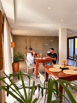 Un comedor con una mesa dispuesta para dos personas, rodeado de plantas en macetas y una pared decorada con palas.
