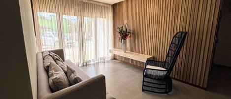 A modern living room with a sofa, a wooden accent wall, a chair, and a small table with a vase of flowers.