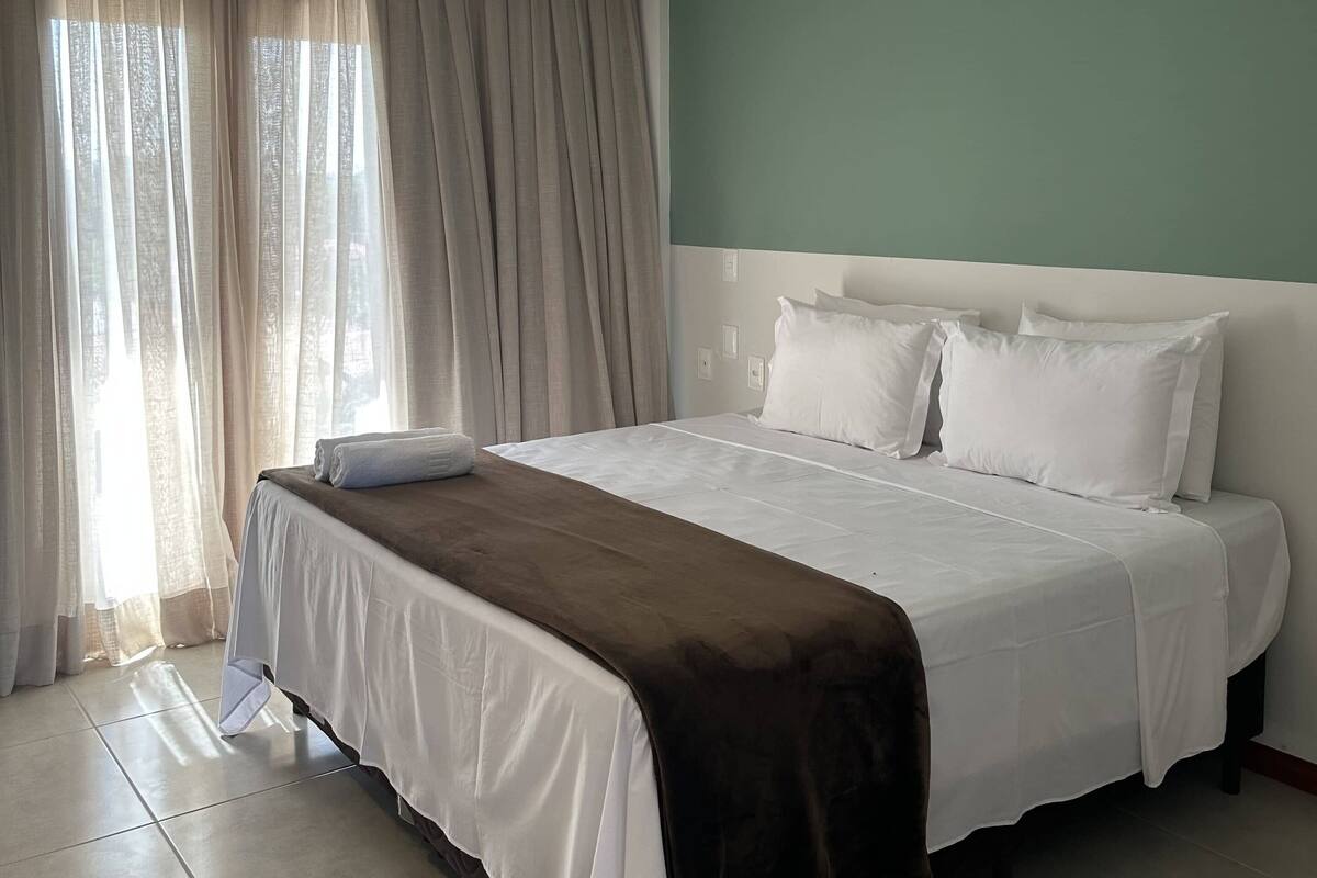 A hotel room with a large bed, beige curtains, and a green accent wall.