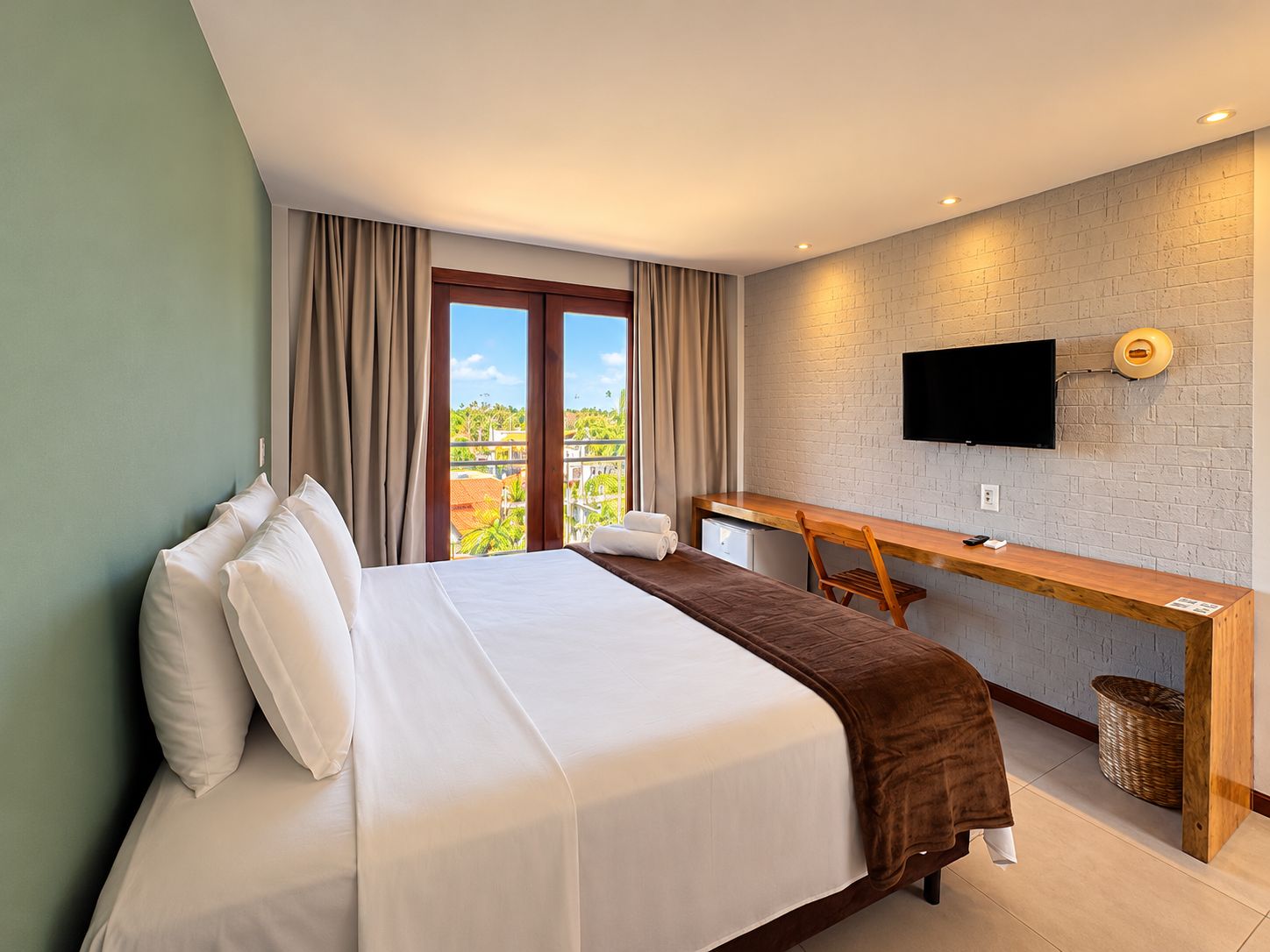 Quarto de hotel com cama, escrivaninha, televisão e vista para o exterior.