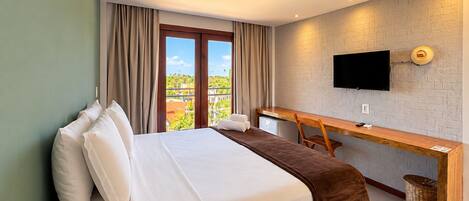 Quarto de hotel com cama, escrivaninha, televisão e vista para o exterior.