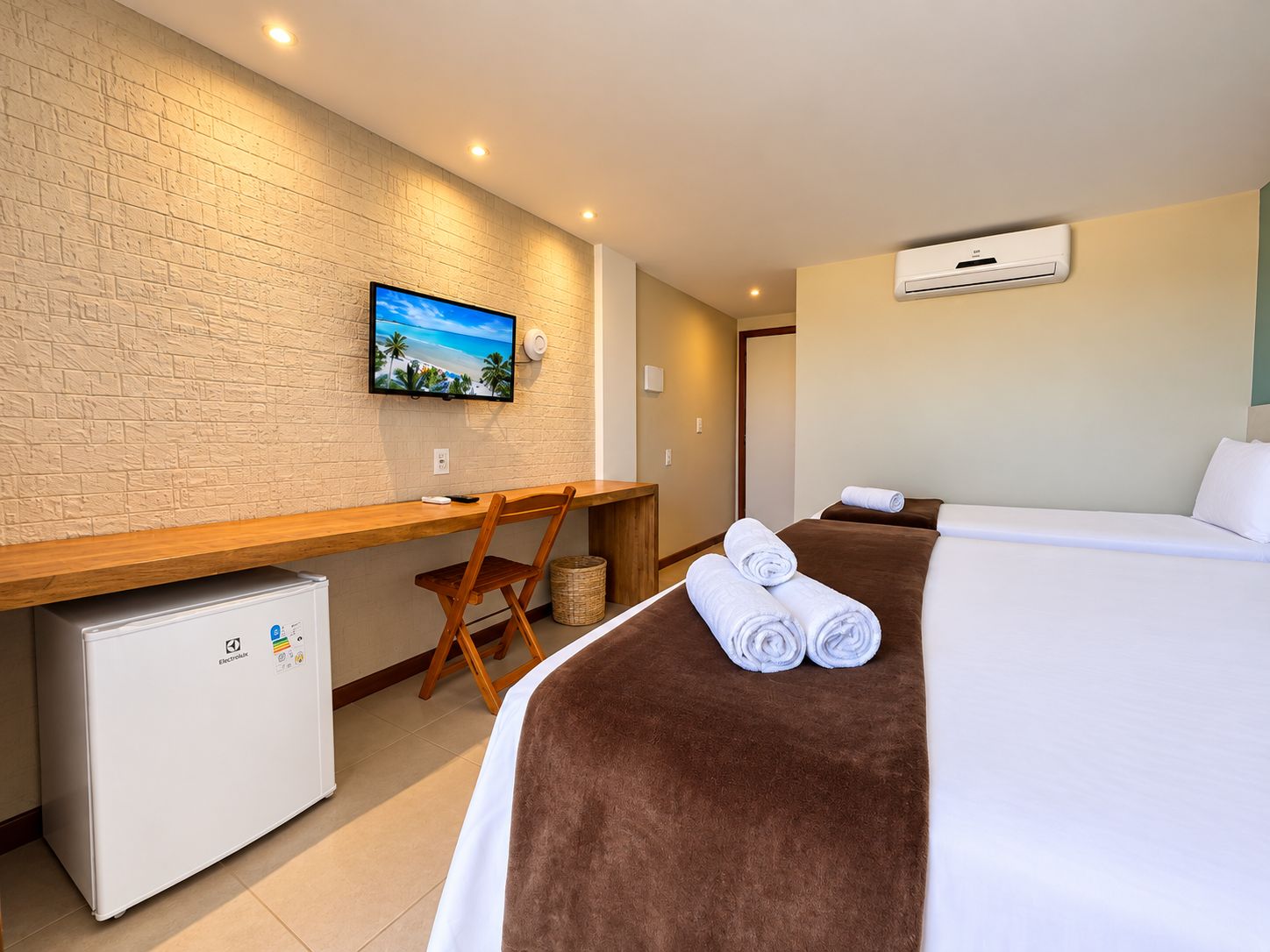 Habitación de hotel con cama, escritorio, televisor, refrigerador y aire acondicionado.