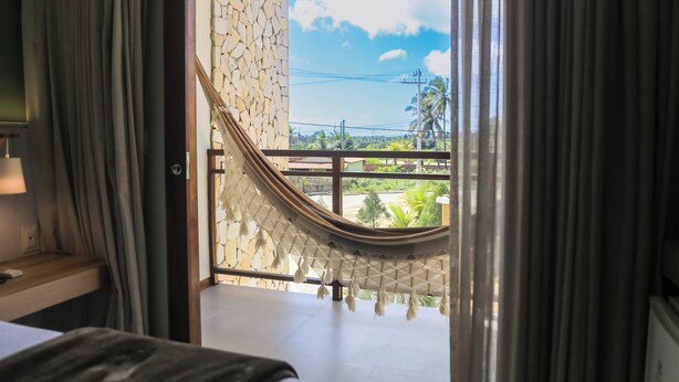 A room with a bed, a window with a view of a balcony, and a hammock. - HOTEL ICARAI BEACH (Amontada)