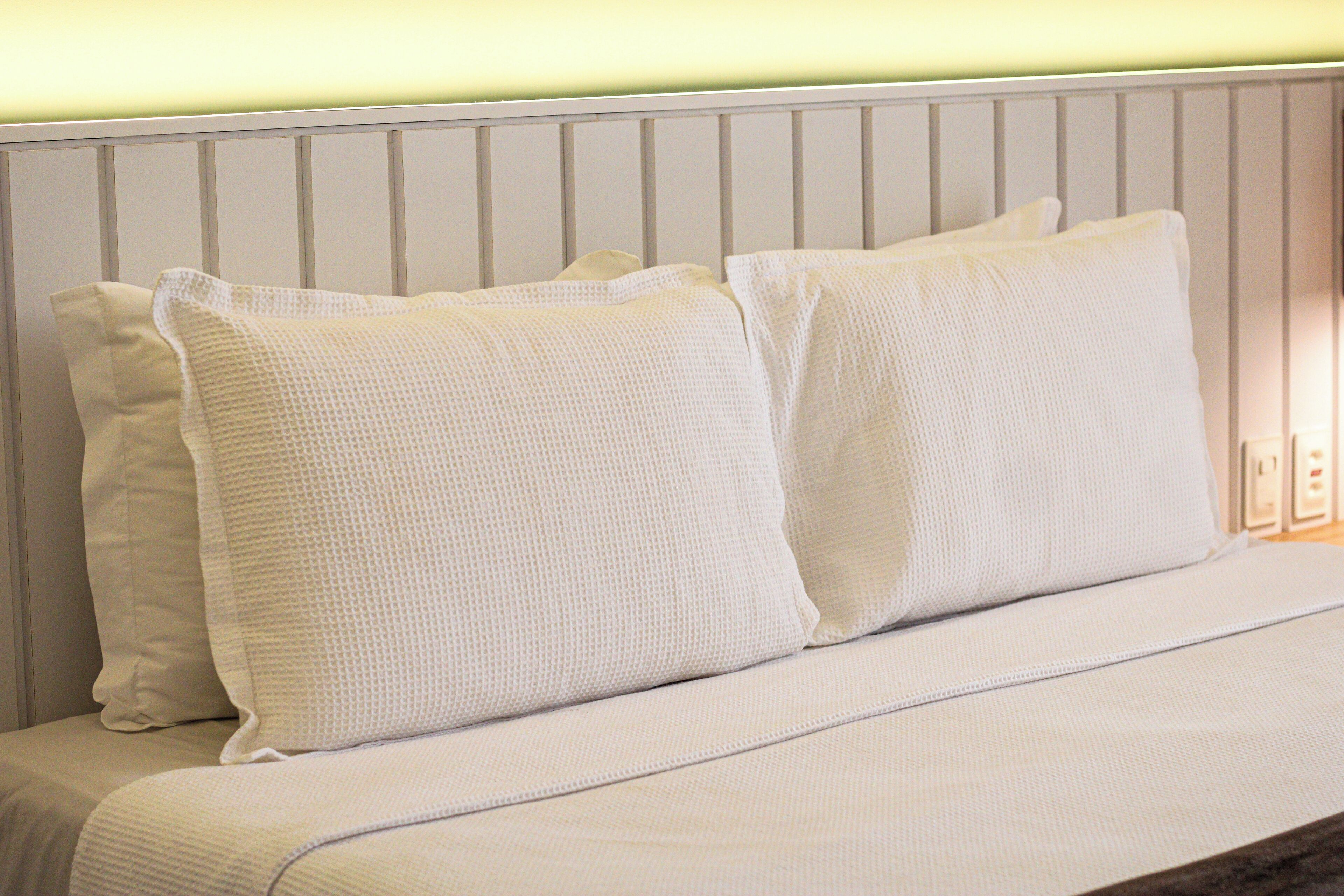 A bed with white bedding and pillows, a white headboard, and a light-colored wall.