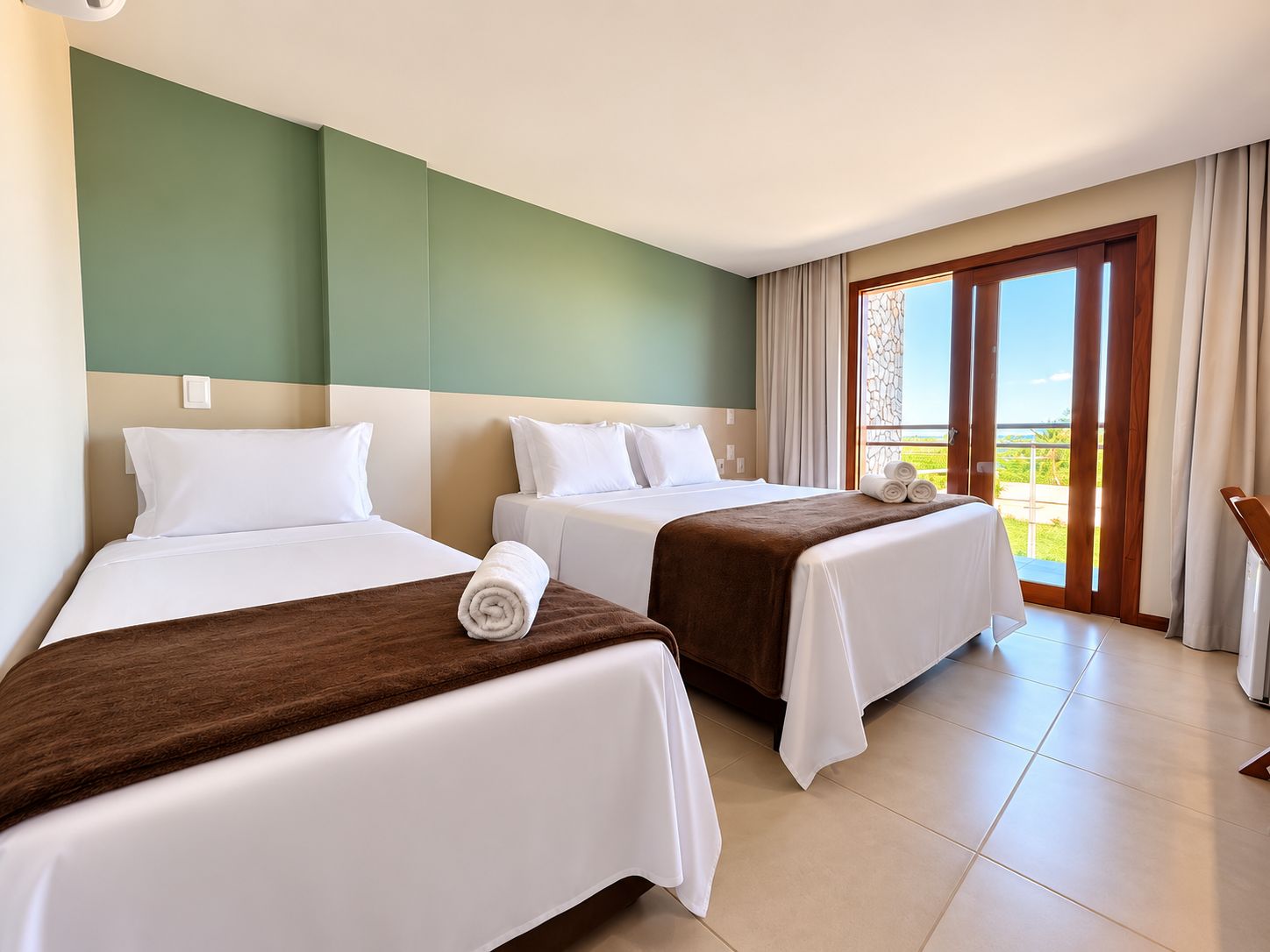 Ein Hotelzimmer mit zwei Betten, einem Balkon mit Vorhängen und Blick ins Freie.