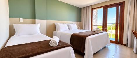Habitación de hotel con dos camas, un balcón con cortinas y vistas al exterior.