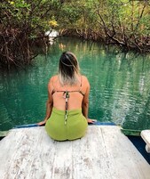 Una persona sentada en un muelle de madera, contemplando una masa de agua rodeada de densa vegetación de mangle.