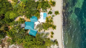 An aerial view of a beachfront property with a swimming pool, multiple rooms with blue roofs, and lush greenery. - Picture-Perfect 2-Bedroom Oceanfront Home w/ Pool (Placencia)