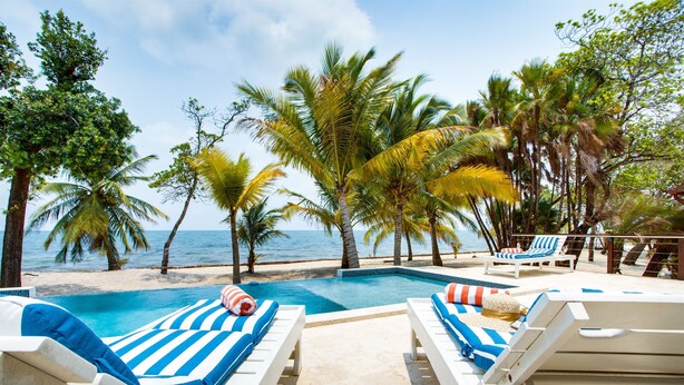 A poolside area with lounge chairs and a view of the ocean. - Hidden Gem: 3-Bedroom Infinity Pool Villa on Beach (Placencia)