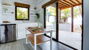 A modern kitchen with white cabinetry, a built-in dishwasher, and a dining area with a wooden table and bench. - Hidden Gem: 3-Bedroom Infinity Pool Villa on Beach (Placencia)
