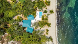 An aerial view of a beachfront property with a swimming pool, multiple rooms with blue roofs, and lush greenery. - Hidden Gem: 3-Bedroom Infinity Pool Villa on Beach (Placencia)