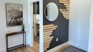 A hallway with a modern art piece, a console table, a mirror, and a wooden wall decoration with a 'Welcome' sign.