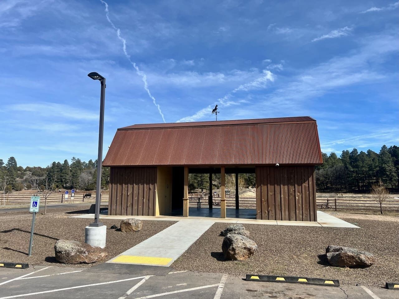 A small, single-story building with a sloped roof, situated in a parking lot with a paved walkway leading to it.