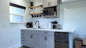 A modern kitchen with grey cabinets, a stainless steel refrigerator, a microwave, and a coffee maker.