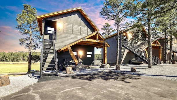 A rustic cabin with a wooden exterior, a staircase leading to the entrance, and a gravel driveway.