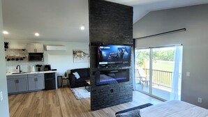 A modern living space with a kitchen, a TV mounted on a stone wall, a balcony with a view, and a large bed.
