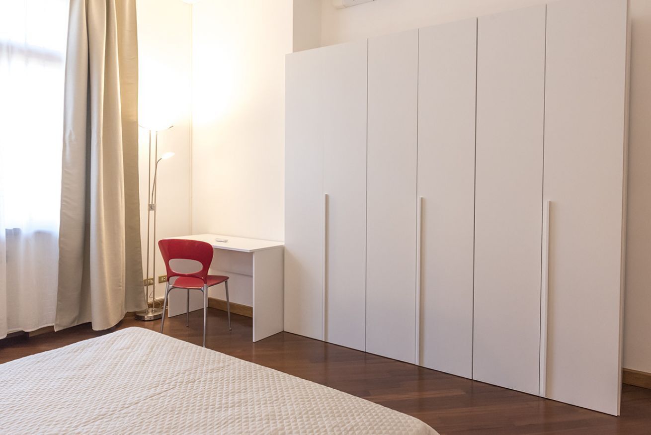 A bedroom with a bed, a desk, a chair, and a wardrobe.