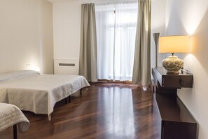 Una habitación de hotel con una cama, un escritorio con lámpara, una ventana con cortinas y un radiador.