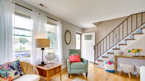 Una sala de estar con sofá, una silla, una lámpara, una alfombra, una escalera y una puerta.