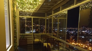 A dining area with tables and chairs, a view of the city at night, and a ceiling adorned with lights and greenery. - Apu Mountain Lodge (Cusco)
