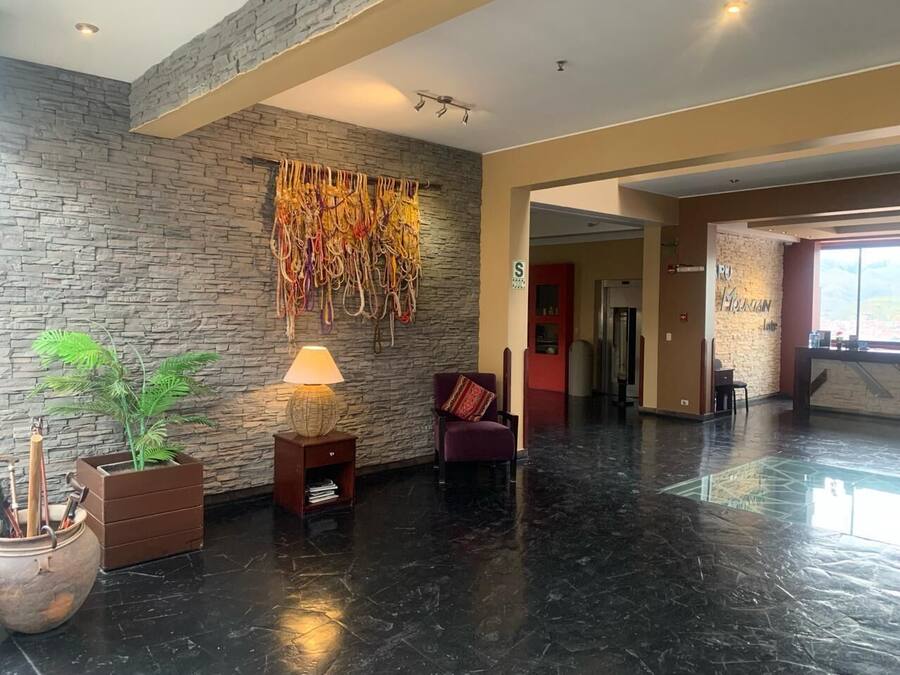 A lobby with a stone wall, a plant, a lamp, a chair, and a reception desk.