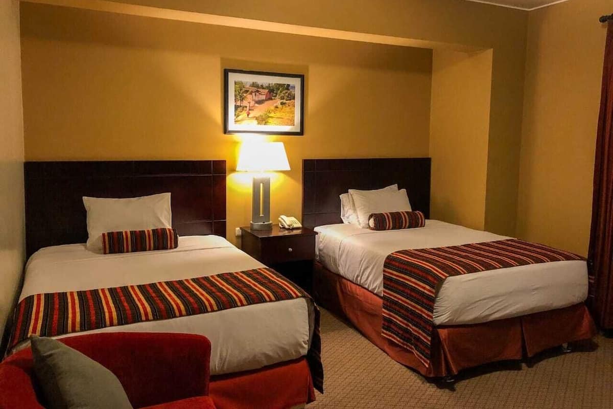 A hotel room with two beds, each with striped bedding and pillows, a nightstand with a lamp, and a framed picture on the wall.