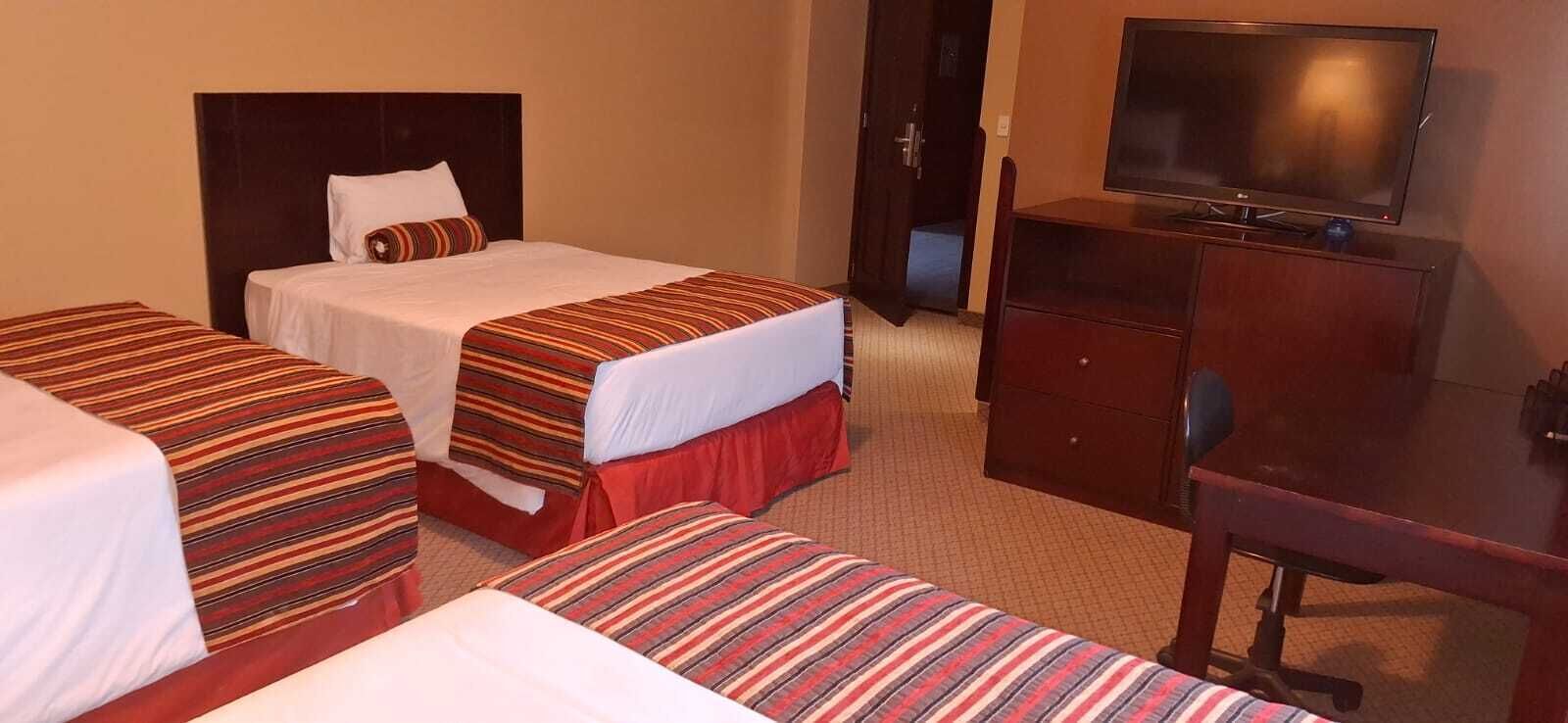 A hotel room with two single beds, a TV, and a wooden dresser.