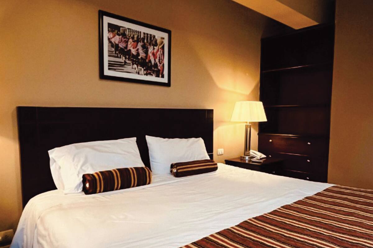 A hotel room with a large bed, a headboard, a nightstand with a lamp, and a framed picture on the wall.