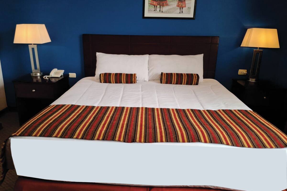 A hotel room with a large bed, two bedside tables with lamps, a framed picture on the wall, and a telephone on one of the tables.