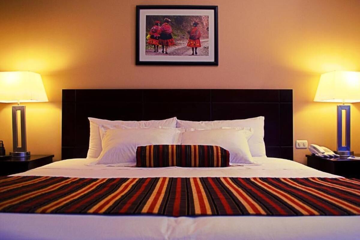 A hotel room with a large bed, two bedside tables, a framed picture on the wall, and two lamps.