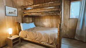 A bunk bed room with wooden walls, a bedside table with a lamp, and a framed picture on the wall.
