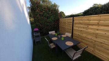 Eine Terrasse mit Tisch und Stühlen, umgeben von einem Holzzaun und einem Heckenstreifen.