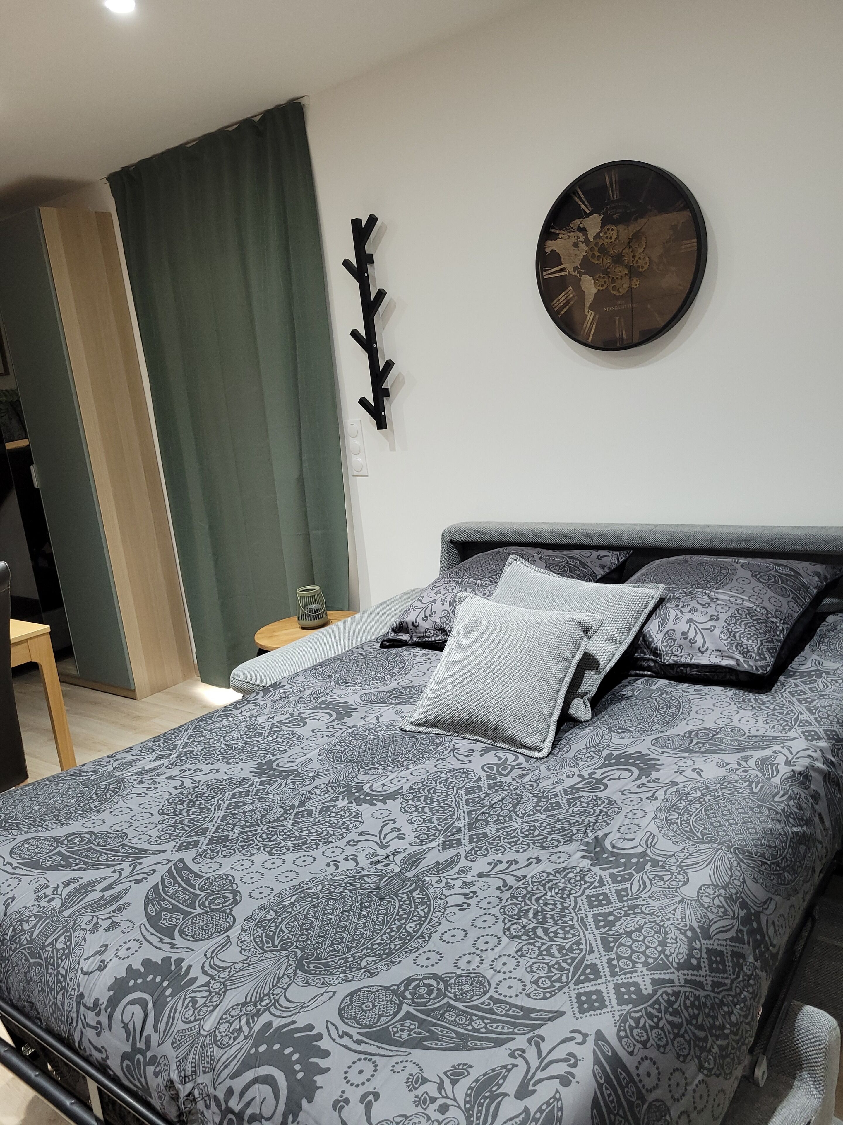 Un dormitorio con una colcha estampada, un reloj de pared redondo y un perchero.