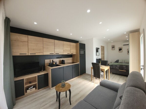 A modern living room with a grey sofa, a wooden coffee table, and a kitchen area with wooden cabinets and a black countertop.