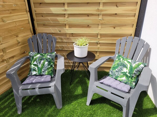 Two grey plastic chairs with leaf-patterned cushions, a small round table, and a potted plant.