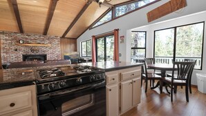 A spacious kitchen with a large island, wooden beams, and a fireplace. - Treetop Falls (Big Bear Lake)