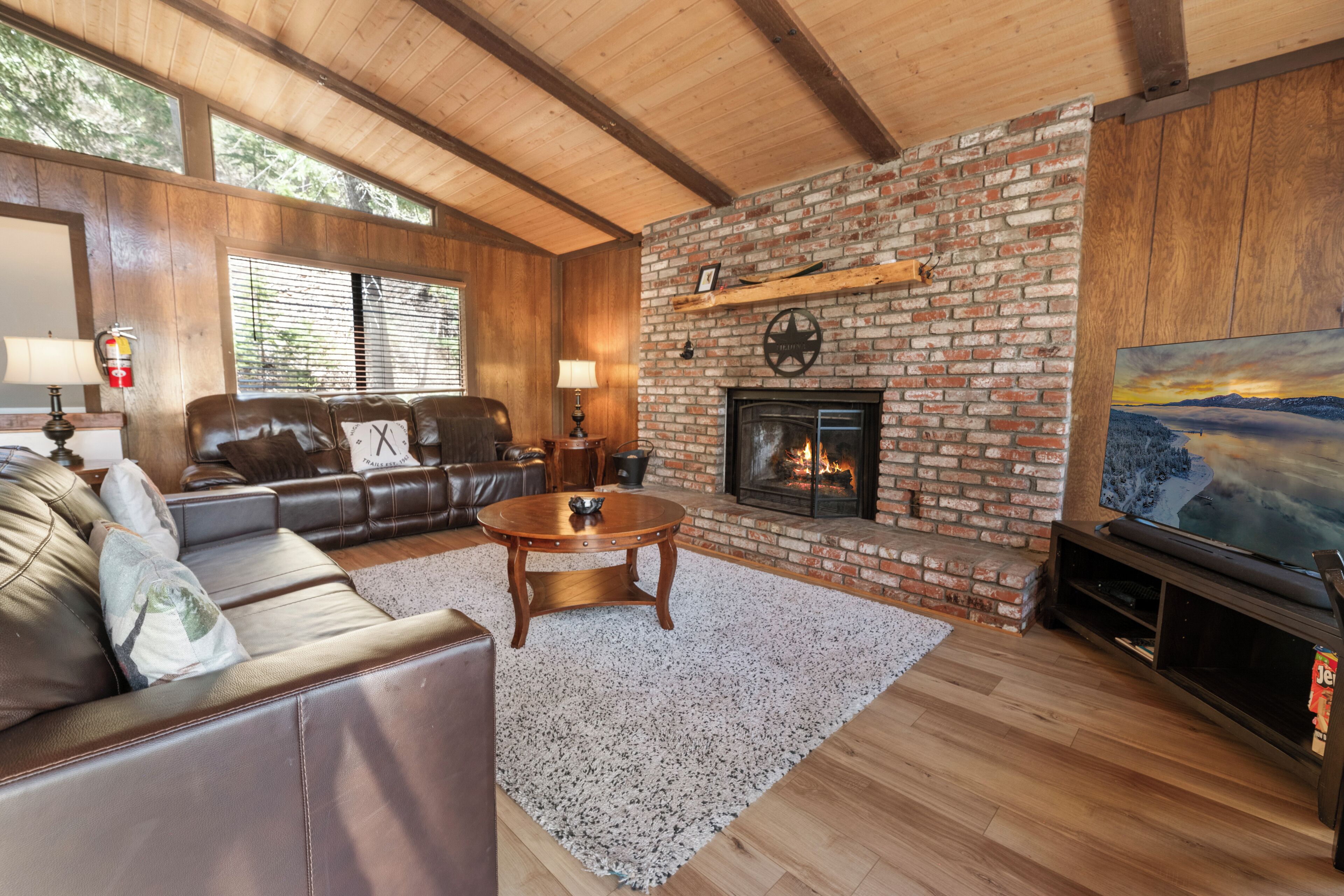 A living room with a brick fireplace, leather sofa, and a flat-screen TV.